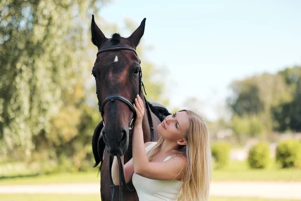 Joven mujer rubia atractiva abraza a un caballo marrón . — Foto de Stock