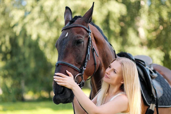 Joven mujer rubia atractiva abraza a un caballo marrón . — Foto de Stock