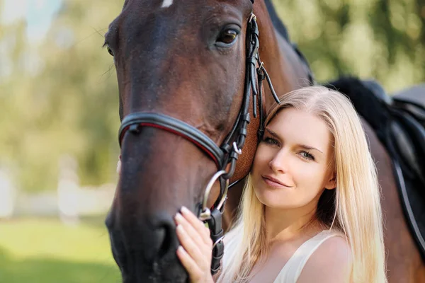 Joven mujer rubia atractiva abraza a un caballo marrón . — Foto de Stock