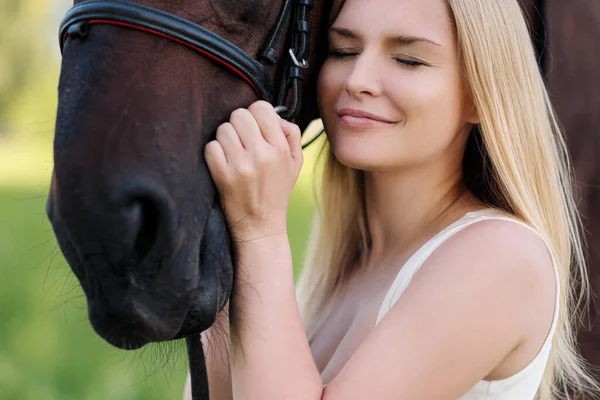 Joven mujer rubia atractiva abraza a un caballo marrón . — Foto de Stock