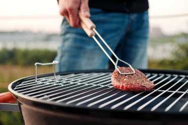 Izgara ızgara. Hamburger için et ve köfte kızartıp eti maşayla çeviren bir adam..