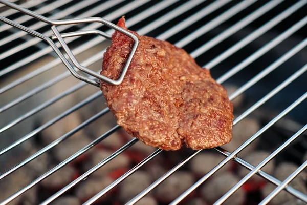 Churrasqueira. Um homem frita bifes de carne e almôndegas para hambúrgueres, vira a carne com pinças. . — Fotografia de Stock