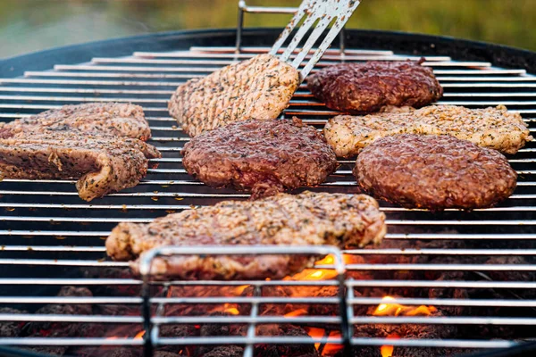 Grill z grilla. Mężczyzna smaży steki mięsne i klopsiki do hamburgerów, przewraca mięso szczypcami. — Zdjęcie stockowe