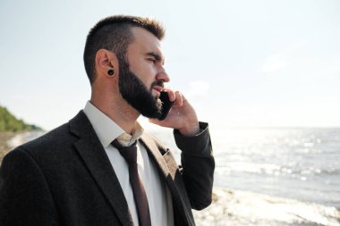 Kahverengi takım elbiseli genç ve çekici bir erkek işadamı deniz kıyısında duruyor. Bağlarını çözer, bağlarını çözer ve ellerini denize kaldırır..