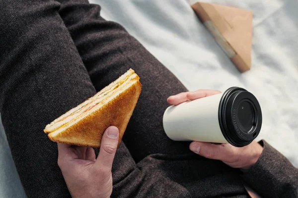 Руки чоловіка в костюмі зі склянкою витягнутої кави і трикутний бутерброд з тунцем . — стокове фото