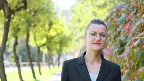 Attractive young business woman in a black jacket and glasses walks and walks along the street outdoors. — Stock Video