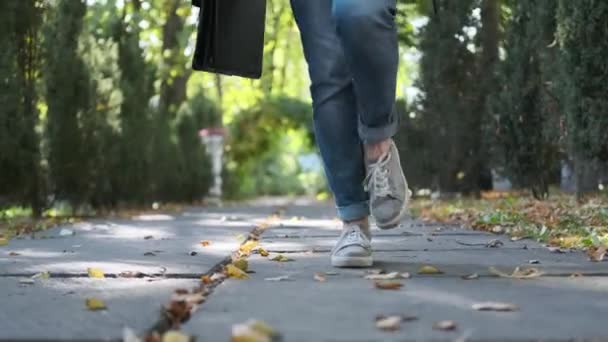 Attractive young business woman with a briefcase in a black jacket and glasses steps, walks and dances outdoors. Rejoices, laughs and has fun in the park. — Stock Video