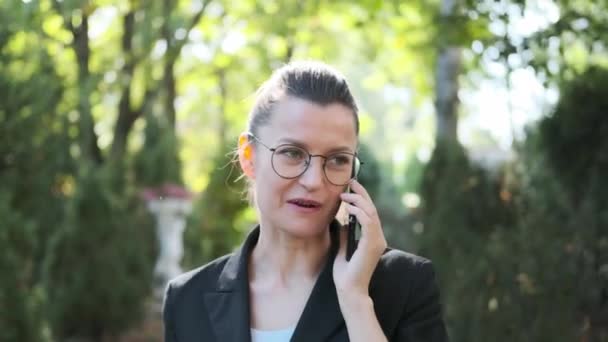 Attractive young business woman with briefcase in black jacket and glasses steps, walks and dances outdoors. Speaks on phone and laughs. Close-up of legs and head. — Stock Video