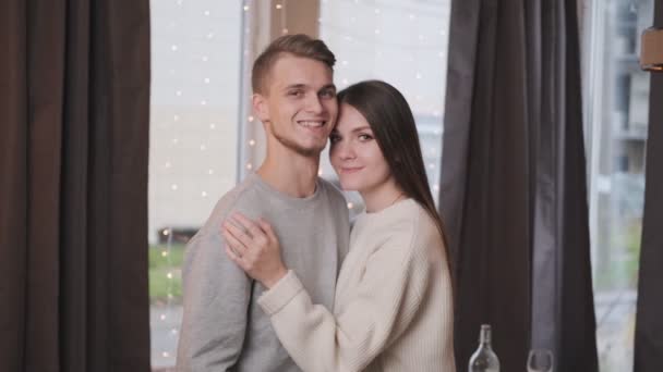 Porträtt av en ung vacker gift par hemma på bakgrunden av en krans och en julgran. — Stockvideo