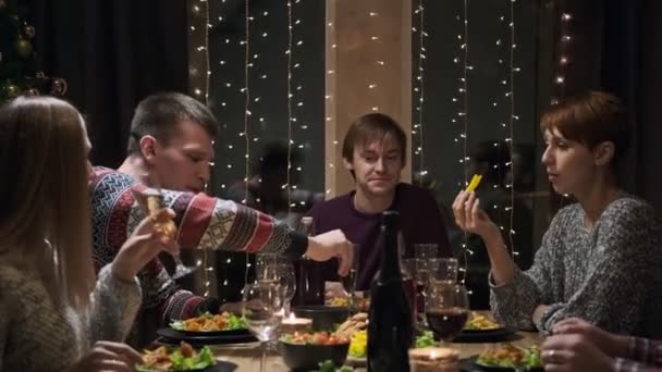 Amigos cena de fiesta en casa alrededor de la mesa. Celebra la Navidad. Cinco personas comen, beben champán, hablan y ríen . — Vídeos de Stock