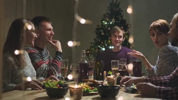 Φίλοι εορταστικό δείπνο στο σπίτι γύρω από το τραπέζι. Γιορτάστε τα Χριστούγεννα. Πέντε άνθρωποι τρώνε, πίνουν σαμπάνια, μιλάνε και γελούν.. — Αρχείο Βίντεο