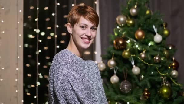 Portret van een jonge mooie vrouw op een achtergrond van de kerstboom. — Stockvideo