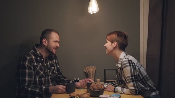 Młoda para małżeńska w luźnych ciuchach, mężczyzna i kobieta, siedzący w domu w kuchni przy stole. Komunikacja duszy i komfort w domu. — Wideo stockowe