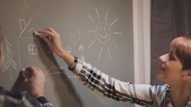 Genç evli bir çift, gündelik giysiler içinde, kadın ve erkek, evlerinde masada oturuyor. Hayallerini duvarda tebeşirle çiz.