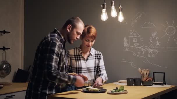 Jong echtpaar in casual kleding, man en vrouw het bereiden van sandwiches thuis in de keuken. — Stockvideo