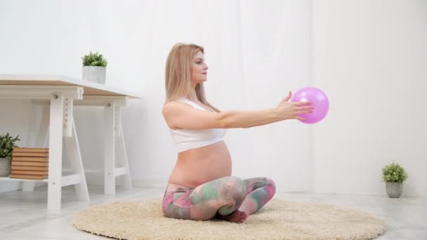 Een jonge mooie zwangere blanke vrouw zit op het zachte tapijt van het huis. Hij is bezig met fitness en oefeningen. Sportkleding. — Stockvideo