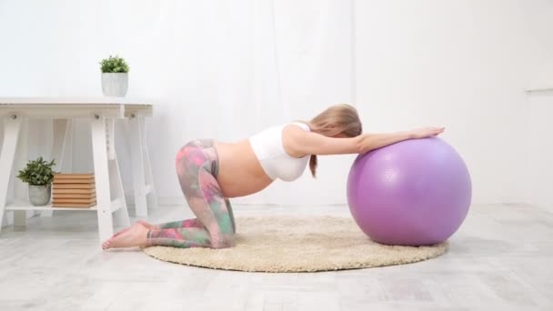 Una giovane donna caucasica incinta si siede sul morbido tappeto della casa. È impegnato in fitness e fare esercizi. Abbigliamento sportivo . — Video Stock