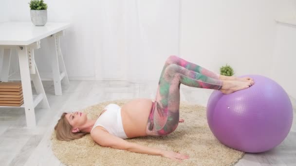 Une jeune belle femme blanche enceinte s'assoit sur le tapis mou de la maison. Il est engagé dans la remise en forme et faire des exercices. Vêtements de sport . — Video