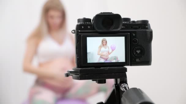 Eine sportliche schwangere junge Bloggerin spricht über Ballübungen. — Stockvideo