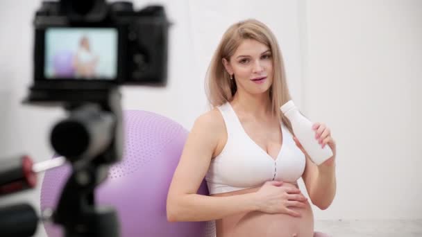 Una joven blogger embarazada deportiva habla sobre ejercicios de pelota . — Vídeo de stock