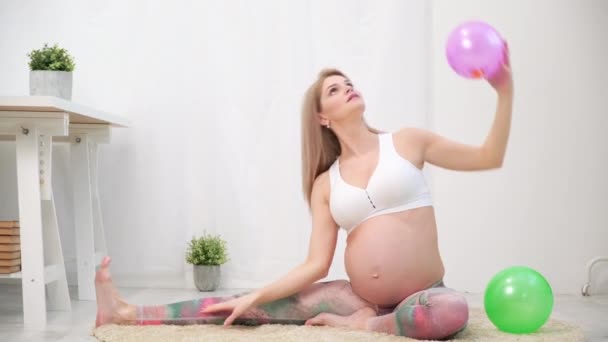 A young beautiful pregnant Caucasian woman sits on the soft carpet of the house. He is engaged in fitness and doing exercises. Sportswear. — Stock Video