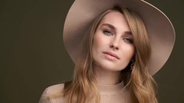 A young beautiful elegant woman in a beige sweater and fedora with fields poses against a green olive background. A close-up of the face. — Stock Video