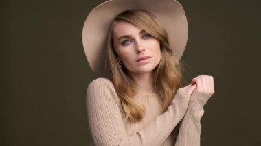 Yeşil zeytin arka planında tarlaları olan bej kazaklı ve fötr şapkalı zarif bir kadın. Yüze yakın çekim..