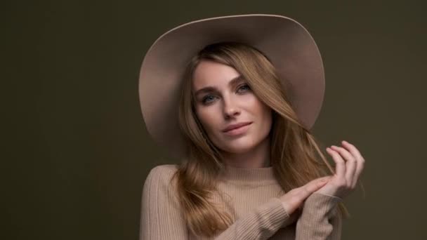Mladá krásná elegantní žena v béžovém svetru a klobouku s poli pózuje na zeleném olivovém pozadí. Detailní záběr na tvář. — Stock video