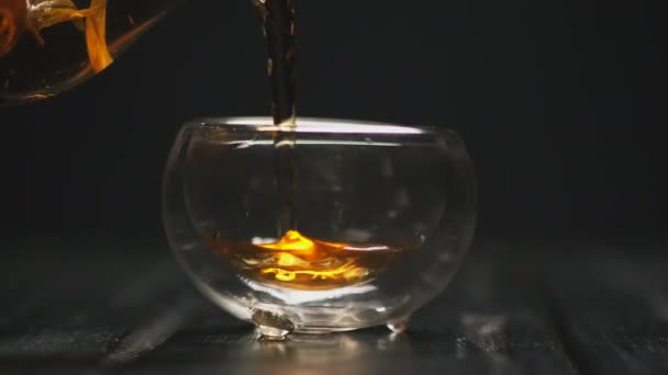 Teezeremonie. Die Frauenhand gießt heißen schwarzen Tee mit Blüten aus einer transparenten Teekanne in gläserne Piala-Tassen. — Stockvideo