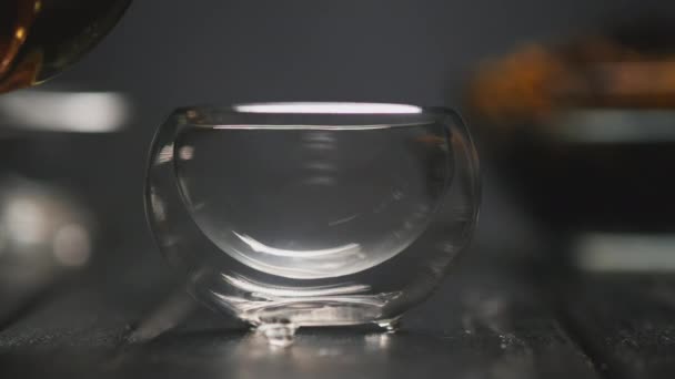 Theeceremonie. De vrouwenhand schenkt hete zwarte thee met bloemen van een transparante theepot in glazen piala kopjes. — Stockvideo
