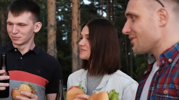 Eine Gruppe von Freunden ruht und entspannt sich in der Natur. Die Menschen essen Hamburger, trinken Bier, kommunizieren und lachen. — Stockvideo