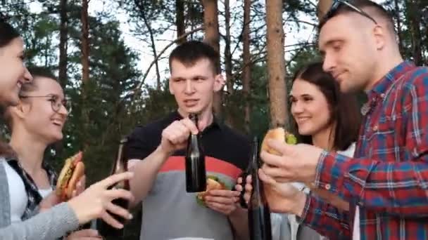 Un grupo de amigos descansa y se relaja en la naturaleza. La gente come hamburguesas, bebe cerveza, se comunica y ríe . — Vídeos de Stock