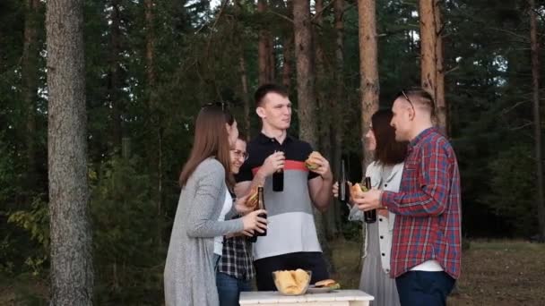 En grupp vänner vilar och kopplar av i naturen. Folk äter hamburgare, dricker öl, kommunicerar och skrattar. — Stockvideo