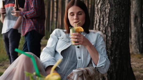 Una giovane donna attraente si rilassa nella natura. Beve un cocktail e comunica con gli amici . — Video Stock