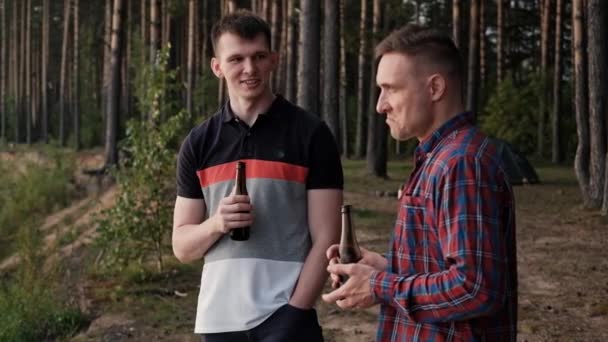 Zwei junge Männer trinken Bier aus Flaschen und entspannen sich im Freien. Ein Wochenende in der Natur, ein Treffen von Freunden. — Stockvideo