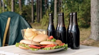 Ormanda açık hava partisi. Kampta akşam yemeği. Şişelenmiş bira ve kokteyller, hamburgerler ve cipsler, abur cubur ve atıştırmalıklar masada..