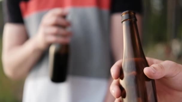 Dos jóvenes beben cerveza de botellas y se relajan al aire libre. Un fin de semana en la naturaleza, una reunión de amigos . — Vídeos de Stock