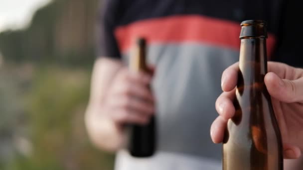 Dos jóvenes beben cerveza de botellas y se relajan al aire libre. Un fin de semana en la naturaleza, una reunión de amigos . — Vídeo de stock