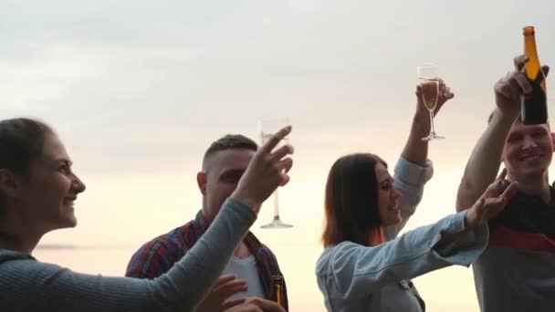 Festa de amigos na praia ao pôr-do-sol. Mulheres e homens se divertem, bebem cerveja e vinho, dançam e riem . — Vídeo de Stock