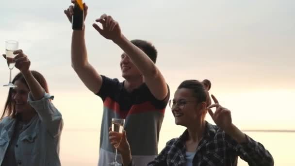 Vänner festar på stranden vid solnedgången. Kvinnor och män har kul, dricker öl och vin, dansar och skrattar. — Stockvideo