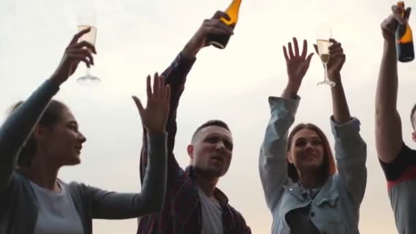 Soirée entre amis sur la plage au coucher du soleil. Femmes et hommes s'amusent, boivent de la bière et du vin, dansent et rient . — Video