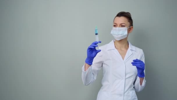 Egy női orvos fehér köpenyben és maszkban egy fecskendőt tart.. — Stock videók