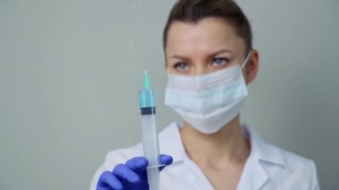 Beyaz cüppeli ve maskeli bir kadın doktor elinde bir şırınga tutuyor..