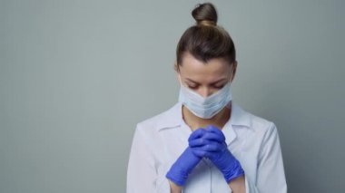 Beyaz cüppeli, maskeli ve eldivenli bir kadın doktor. Yüzü yakın plan. Doktor ağlar ve dua eder. Gözyaşları. Salgın ve virüs salgını. Coronavirus covid-19.