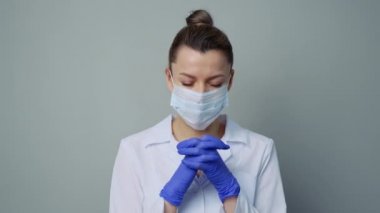 Beyaz cüppeli, maskeli ve eldivenli bir kadın doktor. Yüzü yakın plan. Doktor ağlar ve dua eder. Gözyaşları. Salgın ve virüs salgını. Coronavirus covid-19.