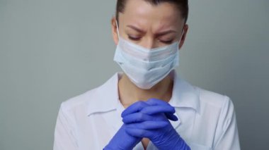 Beyaz cüppeli, maskeli ve eldivenli bir kadın doktor. Yüzü yakın plan. Doktor ağlar ve dua eder. Gözyaşları. Salgın ve virüs salgını. Coronavirus covid-19.