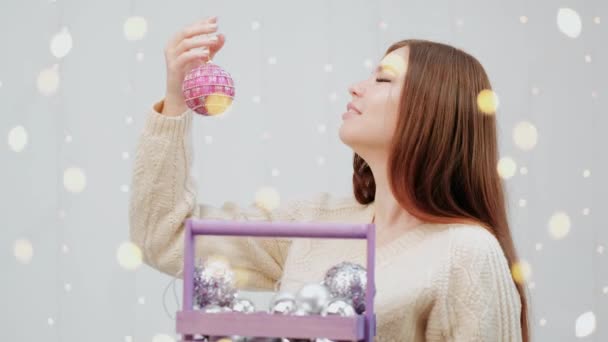 Porträt eines Mädchens auf weißem Hintergrund. Eine Schachtel Spielzeug für den Weihnachtsbaum. — Stockvideo