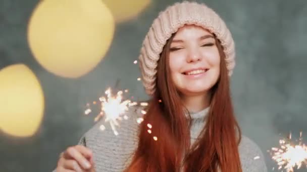 Aranyos lány meleg pulcsiban és kötött sapkában felgyújtja a csillagszórókat és az örömöket. Homályos fények. — Stock videók