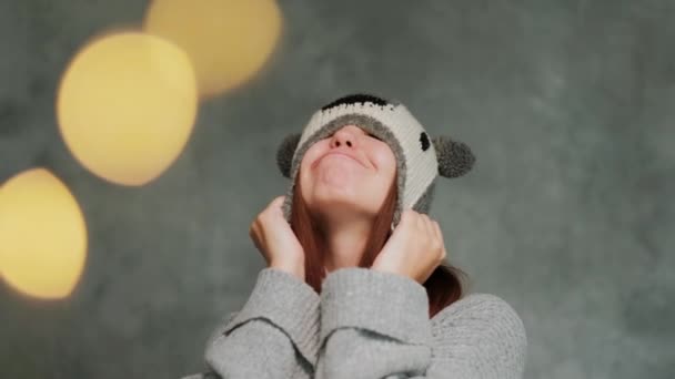 Chica atractiva en un suéter de punto de invierno y un sombrero con un koala se divierte y posa sobre un fondo gris . — Vídeo de stock