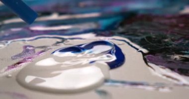 Bir kadın sanatçı yağlı boya ile soyut bir tablo çizer. Bir değnekle akışkan çizim. Beyaz bir tuvalde parlak boya..